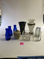 Front view of all nine vases arranged on a white background, showing colors and shapes ranging from blue ceramic to various glass styles.