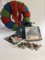 Photo showing Christmas cloth wreath, plastic tree stand, nativity bake set box, and Christmas-themed knives lined in front