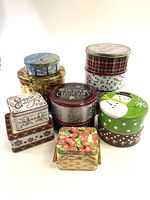 Overview photo showing 9 assorted Christmas and decorative cookie tins arranged in two rows, featuring varied holiday designs and colors.