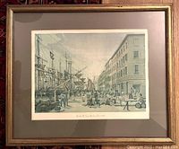 Framed hand tinted print showing a harbor street scene with ships, barrels and people in historic dress.