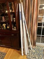 Five new Kirsch curtain rods in original boxes leaning against a cabinet next to a used drapery rod.