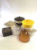 Full view of all plastic kitchenware items including two cheese covers, recipe box, yellow and white baking trays, white divided plate with cover, and white rack.