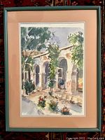 Framed watercolor painting showing architectural arches, plants in the courtyard, pencil signed by the artist. Frame condition shows matting and slight slip of the print inside.