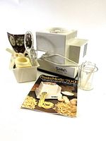 Image shows the PastaMatic 700 machine, multiple attachments in a container, measuring cup, stirring tool, and instruction manual laid out on a white surface.