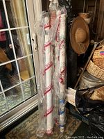 Four rolls of fabric standing upright, covered in branded plastic wrapping, near a door and household items.