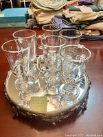 Front angle view showing six clear Irish coffee glasses arranged on the vintage brass framed round mirror with beveled edge on a table surface.