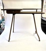 Front view of the vintage folding sewing table showing laminated wood top, drawer, and foldable metal legs