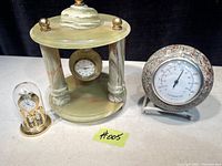 Full view of both clocks and thermometer on a white table with black background.