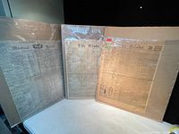Photo showing three antique newspaper front pages wrapped and displayed upright, titled Montreal Herald, The Globe and Mail, and The Globe