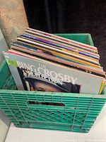 View of 41 vinyl records standing vertically in a green crate showing a variety of album cover edges, titles and colors.