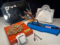 Photo of the lot items showing the match holder, trivet, wood box with metal decoration, pipe cleaning tools, and blue ankle weight.