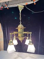 Full fixture view, lit, against black backdrop, showing four frosted glass pyramid shades, brass arms, and central column.