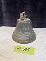 Front view of the antique bronze bell showing the year '1878' and partial inscription 'SAIGNELEGIER'. The bell has a square-shaped handle and green patina from oxidation.
