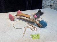 Photo of the antique metal pull toy for kids showing its construction, painted metal body, wheels, and pull string on a light surface with stone background.