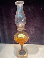 Full view of the antique oil lamp showing the amber glass reservoir, tall clear chimney, metal burner, and marble base.