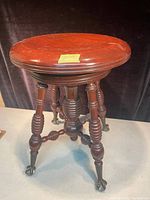 Front view of antique organ stool showing round wooden seat and ornate turned legs ending in cast iron claw and glass ball feet.