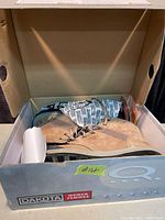 Side view of tan suede Dakota women's winter boots in original box, showing lace-up closure and rubber sole.