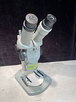 Photo showing front view of the microscope with dual eyepieces and metal base with slide clips.