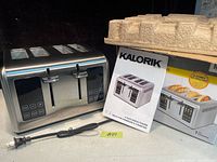 Kalorik stainless steel 4-slice toaster with original packaging and manual. Power cord visible, unit in new condition.