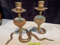 Pair of vintage brass cobra-shaped candle holders shown from front angle displaying etched detailing and coiled bodies.