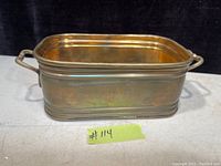 Rectangular solid brass vintage planter with handles on each side shown on a white surface against a black background. The planter has a polished surface with minor patina, highlighting its vintage nature.