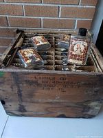 Original cardboard shipping crate containing 36 individual compartments holding the glass bottles. Crate is marked with printing on the side and shows age wear.