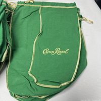 Green Crown Royal whiskey bottle bags featuring gold stitching and drawstring, stacked neatly.
