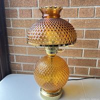 Full view of amber hobnail glass hurricane lamp showing the dome shade with ruffled edge and round base with hobnail pattern.