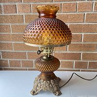 Front view of amber hobnail glass lamp showing textured glass shade and base, ornate metal base, and electric cord.