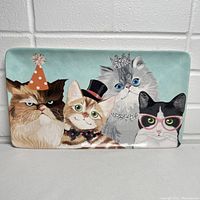 Full front view of rectangular ceramic tray with four illustrated cats wearing party attire: party hat, top hat, tiara, pink rhinestone glasses, set against a turquoise background.