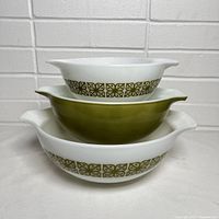 Three vintage Pyrex Verde Square Flowers pattern Cinderella bowls stacked in descending size, white bowls with green floral band and a solid olive green bowl in the center.