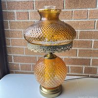 Full view of vintage amber hobnail hurricane lamp showing the textured glass globe and shade with decorative metal trim, brass base, and power cord.