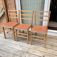 Front view of three wood folding chairs with ladder backs and brown vinyl seats, showing overall condition and style.