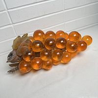 Full view of the large vintage amber Lucite grape cluster laid flat, showing the translucent spherical grapes and metal leaves on one side.