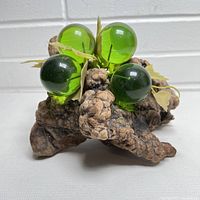 Front angle view of the MCM Lucite grapes on driftwood showing three green translucent Lucite grapes with attached cream-colored leaf decorations on a rugged driftwood base.