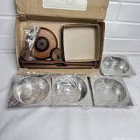 Photo showing all the server set parts laid out including bowls wrapped in plastic, wooden crossbars, round base parts, cocktail forks, and small box containing screws or fittings.