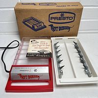 Presto Hot Dogger cooker, parts separated showing base, skewers and manual with box in background.