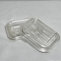 Two vintage Pyrex small clear glass lids stacked at an angle showing ribbed rectangular design and curved edges.