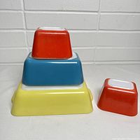 Three Pyrex refrigerator storage dishes stacked: solid red, blue, and yellow colors.