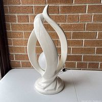 Front view of white ceramic flame lamp on table against brick wall