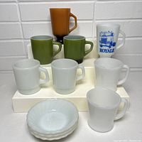 Photo showing all 8 mugs and 3 small dishes together on white platform against tiled background.