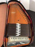 Full view of the Oscar Schmidt autoharp resting inside a padded case showing the strings, chord bars, and piano key markings on the soundboard.