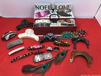 Overview of assorted hair clips, barrettes, and claw clips arranged on red background with box labeled 'NOEL LOVE'