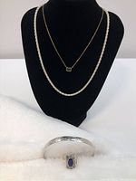 Silver and gold-colored chain necklaces and silver ring and bangle displayed on black and white cloth backgrounds.