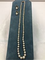 Full view of necklace and earrings on blue background showcasing pearls and clasp