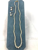 Pearl necklace with graduated pearls laid on a blue display board alongside matching clip-on pearl earrings.