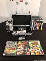 Open aluminum carrying case with foam compartments, PS2 cables and extra compartments visible, PSP and PS2 games stacked on either side