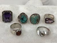 Six sterling silver rings laid out on white foam background showing various stones: amethyst, amber, turquoise, and marcasite embellishments.