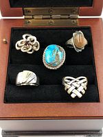 Five silver rings in wooden box, various designs including turquoise, moss agate, garnet, geometric and heart motif.