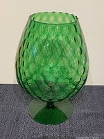 Front view of large emerald green textured glass snifter showing optic bubble pattern and pedestal base.